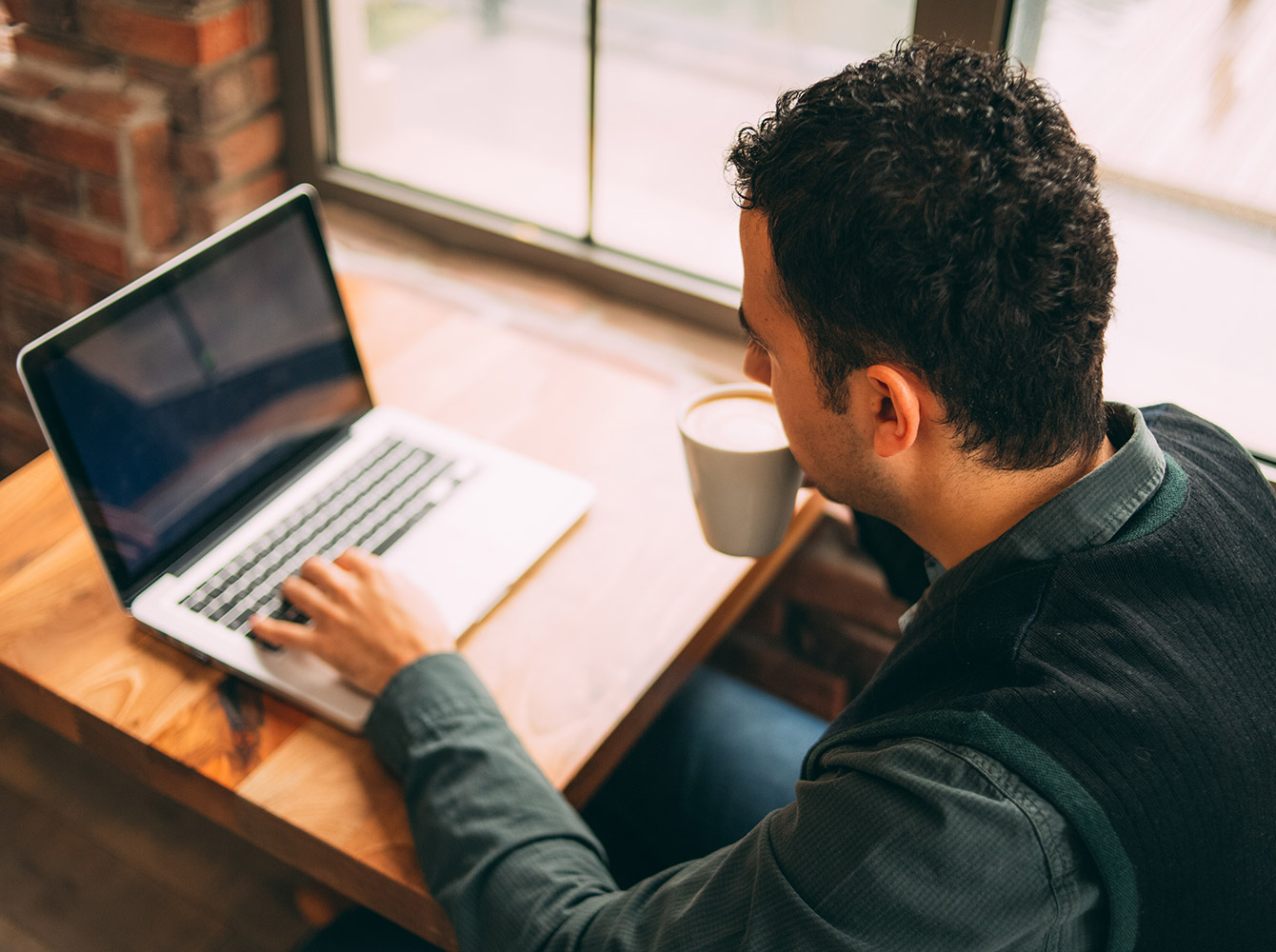 Man drinking coffee and typing on a laptop