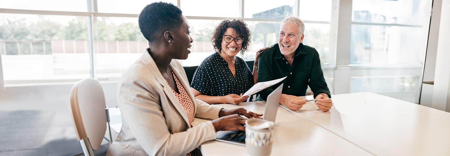 Three people are sitting and smiling while discussing paperwork.