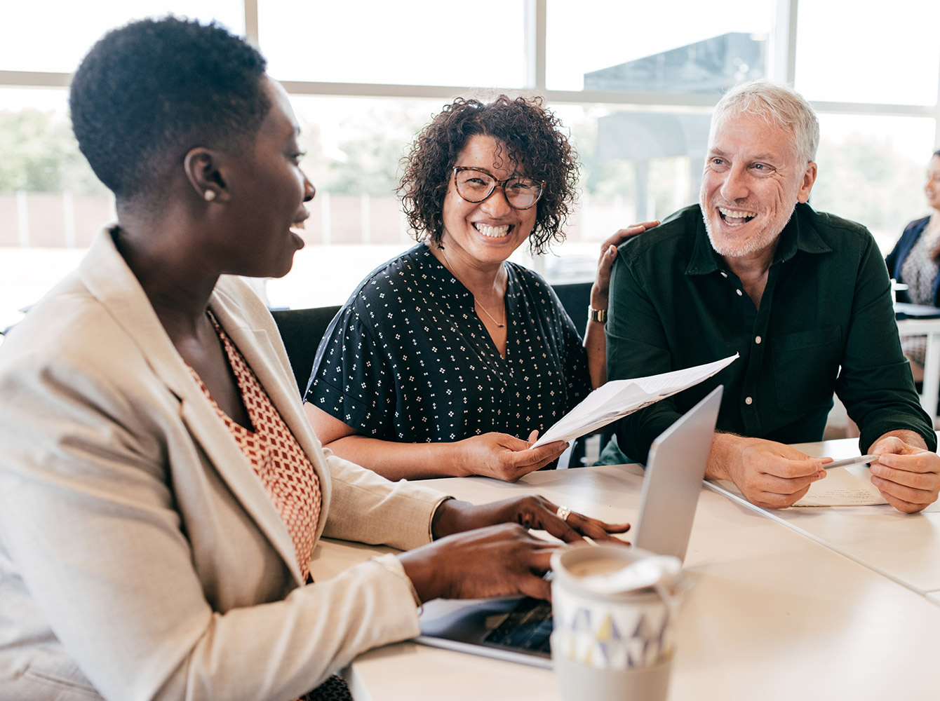 Three people are sitting and smiling while discussing paperwork.