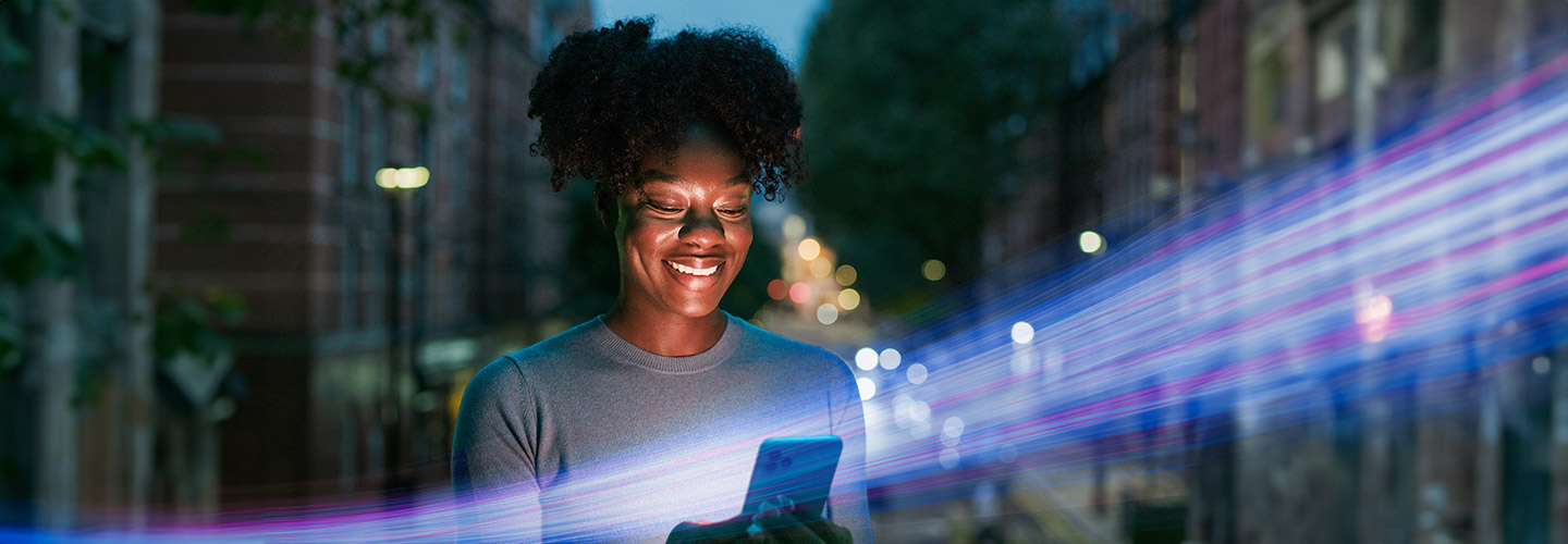 A woman is looking at her cell phone in her hands and smiling.