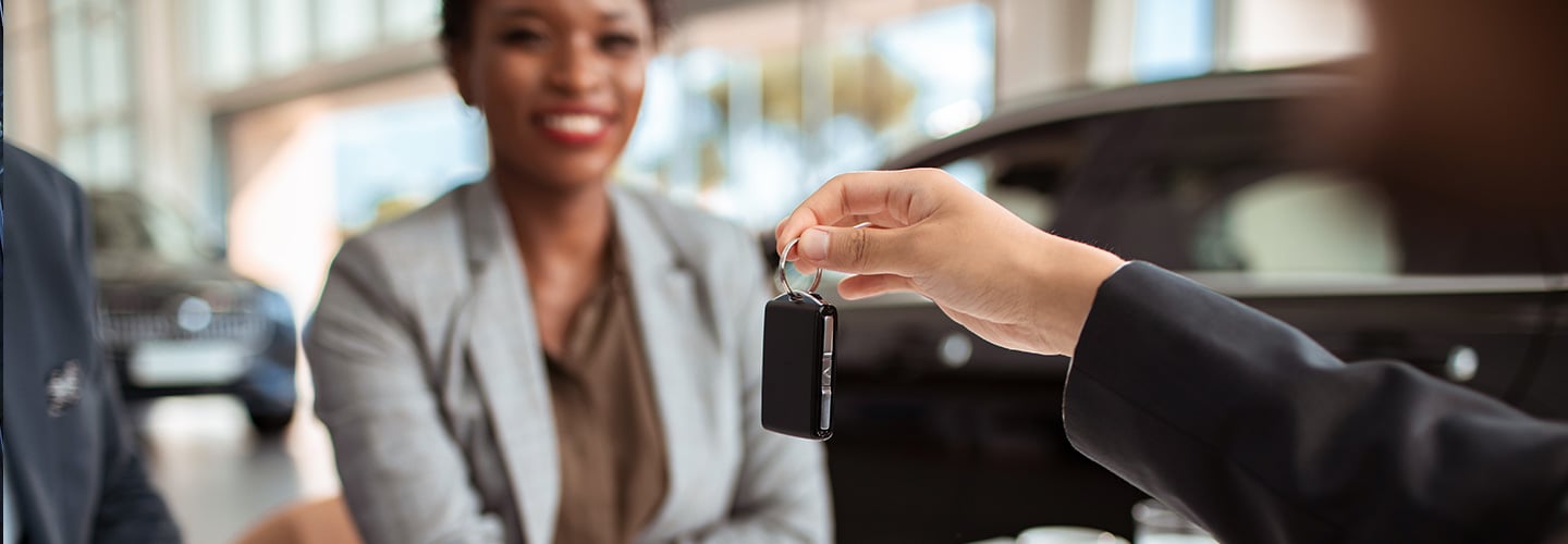 a smiling woman with papers laid out in front of her is being handed car keys