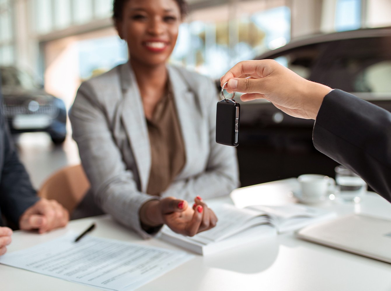 a smiling woman with papers laid out in front of her is being handed car keys