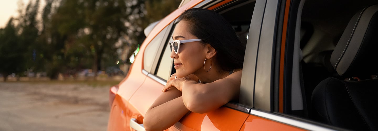 woman with sunglasses on leaning out the rolled down back window of a car