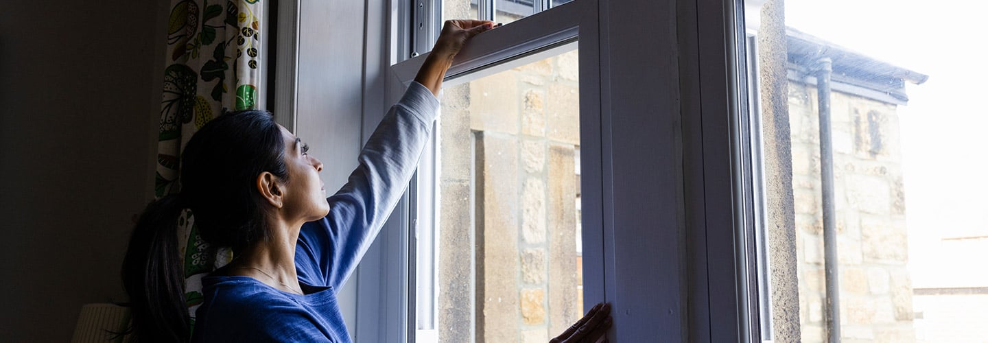 A woman reaching up to unlock a window in a house