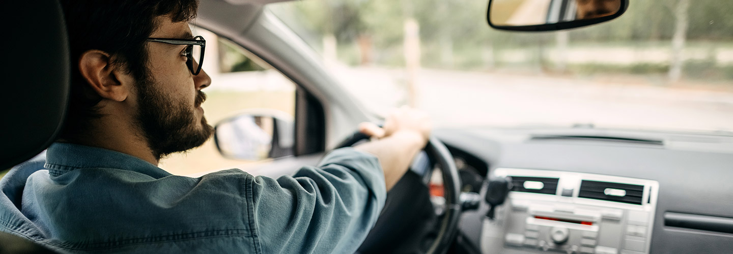 A man sits in the driver's seat of a car with his hands on the wheel.