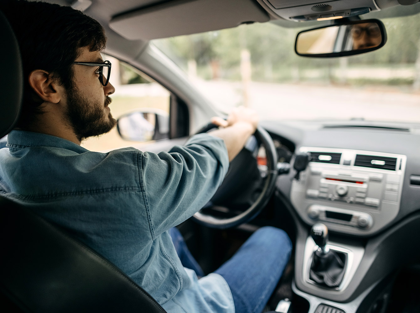 A man sits in the driver's seat of a car with his hands on the wheel.