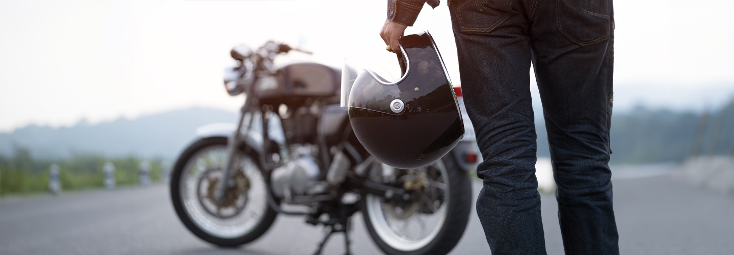 A person is walking towards a parked motorcycle with a helmet in their hand.