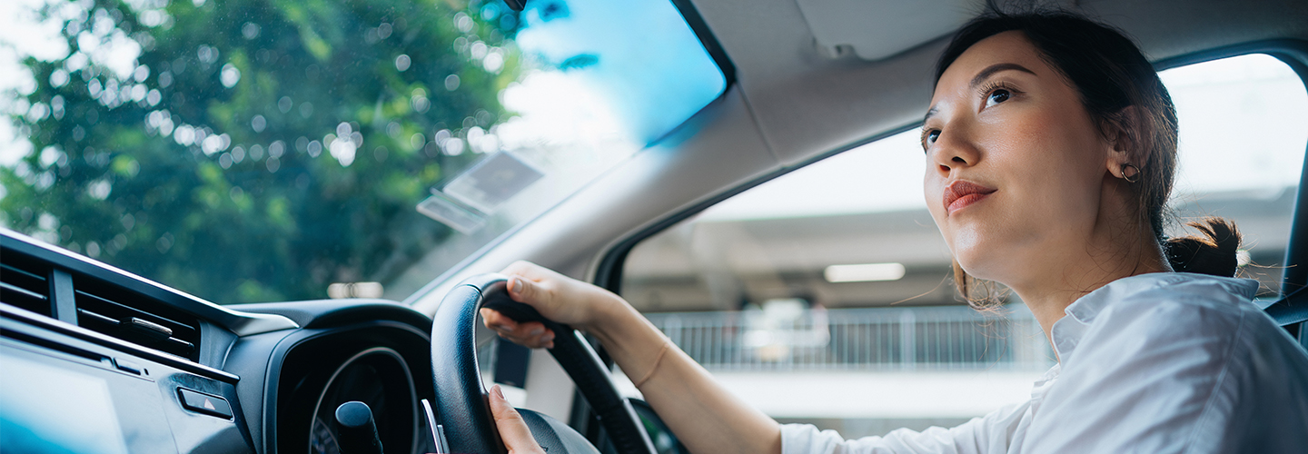 A woman is behind the wheel of a car on a nice day.