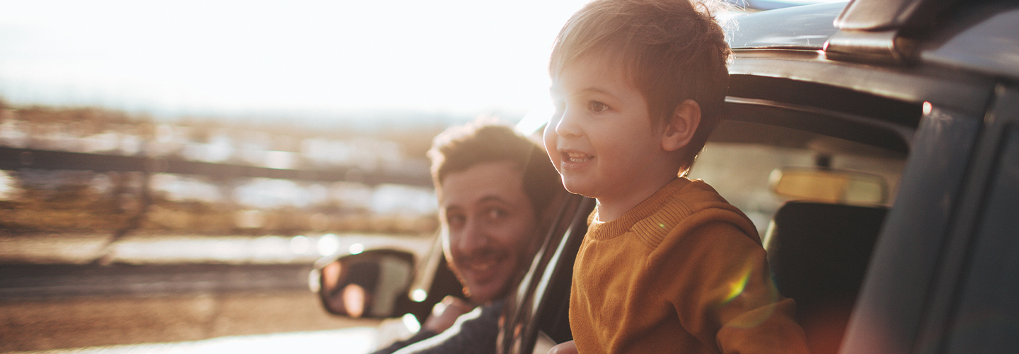 A father and son are sticking their heads out of a car window on a sunny day.
