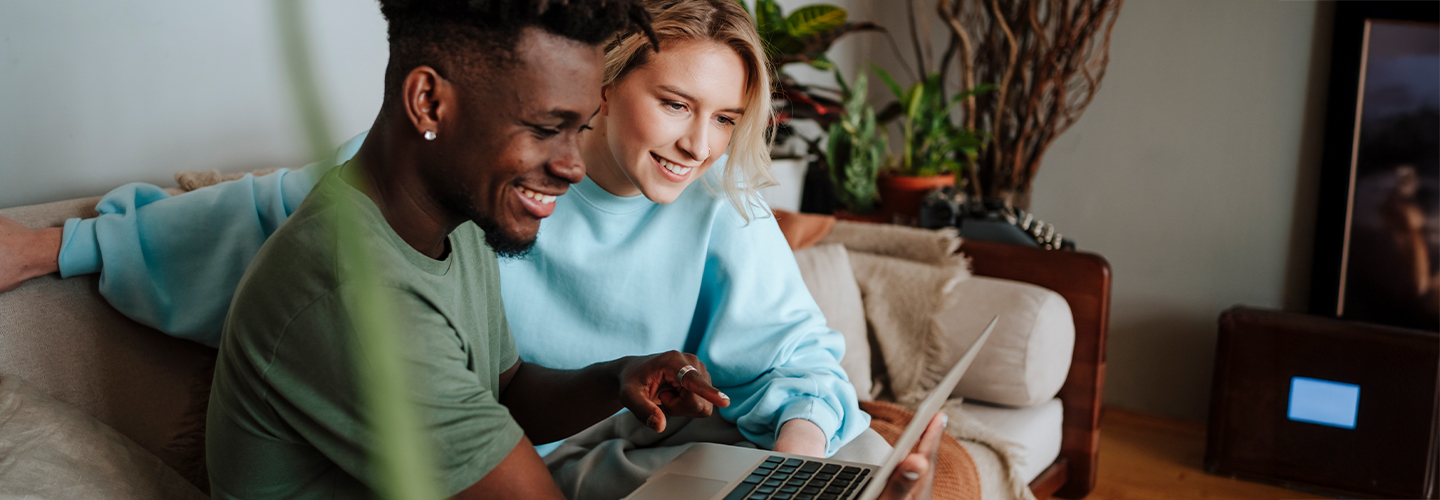 A couple sits together on the couch while looking at a laptop.