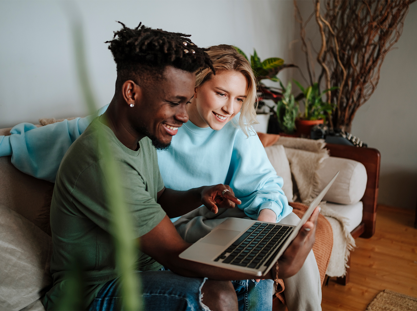A couple sits together on the couch while looking at a laptop.