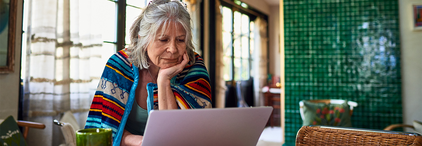 A woman is sitting at her table looking at a laptop.