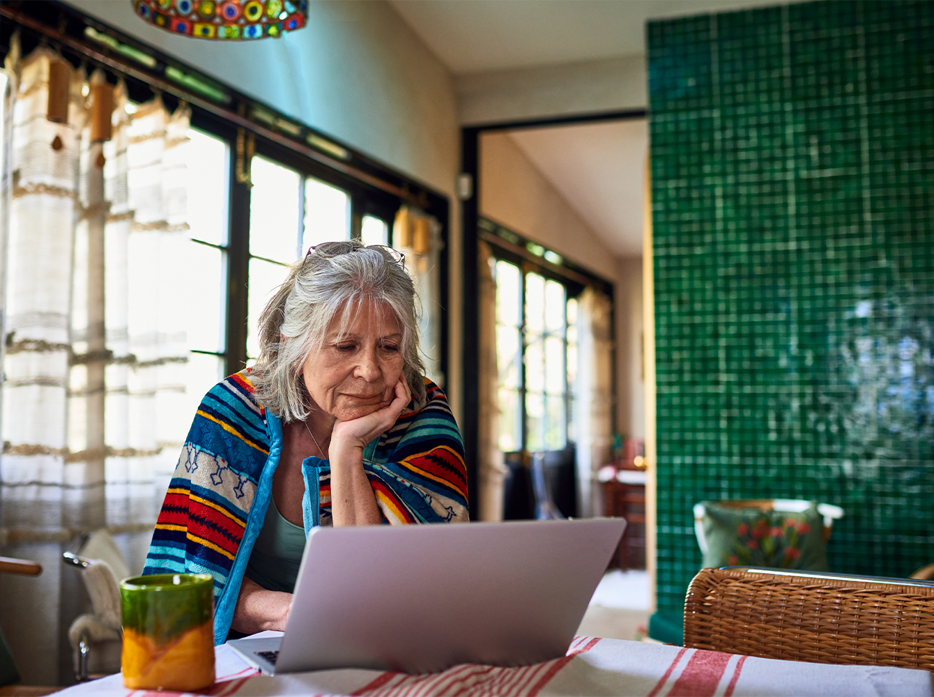 A woman is sitting at her table looking at a laptop.