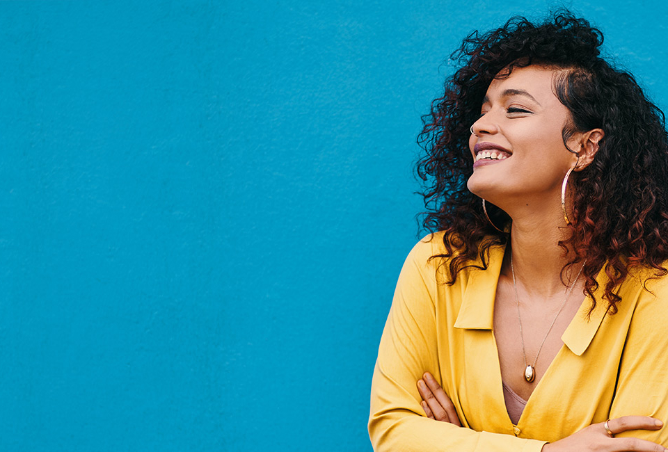 Woman smiling wearing a yellow shirt against a blue background