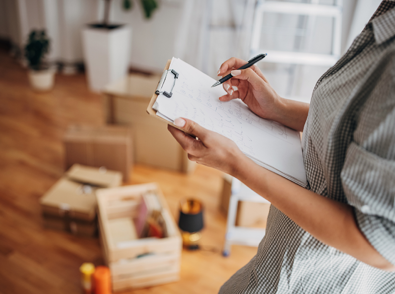 A person writing on a clipboard while inventorying belongings in a room with open boxes on the floor.