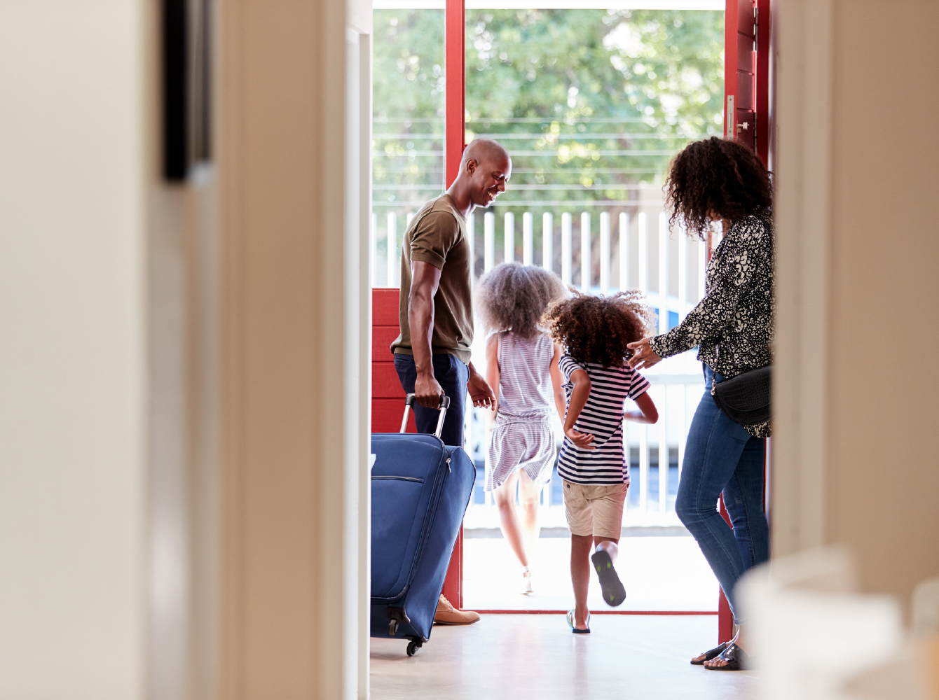 A family with two young children and a suitcase heading out the front door for a trip.