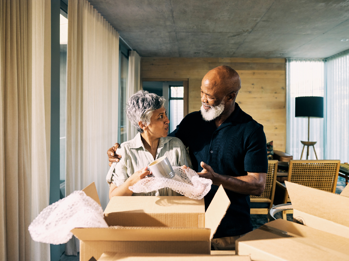 An older couple packs or unpacks moving boxes together in a bright modern living space.