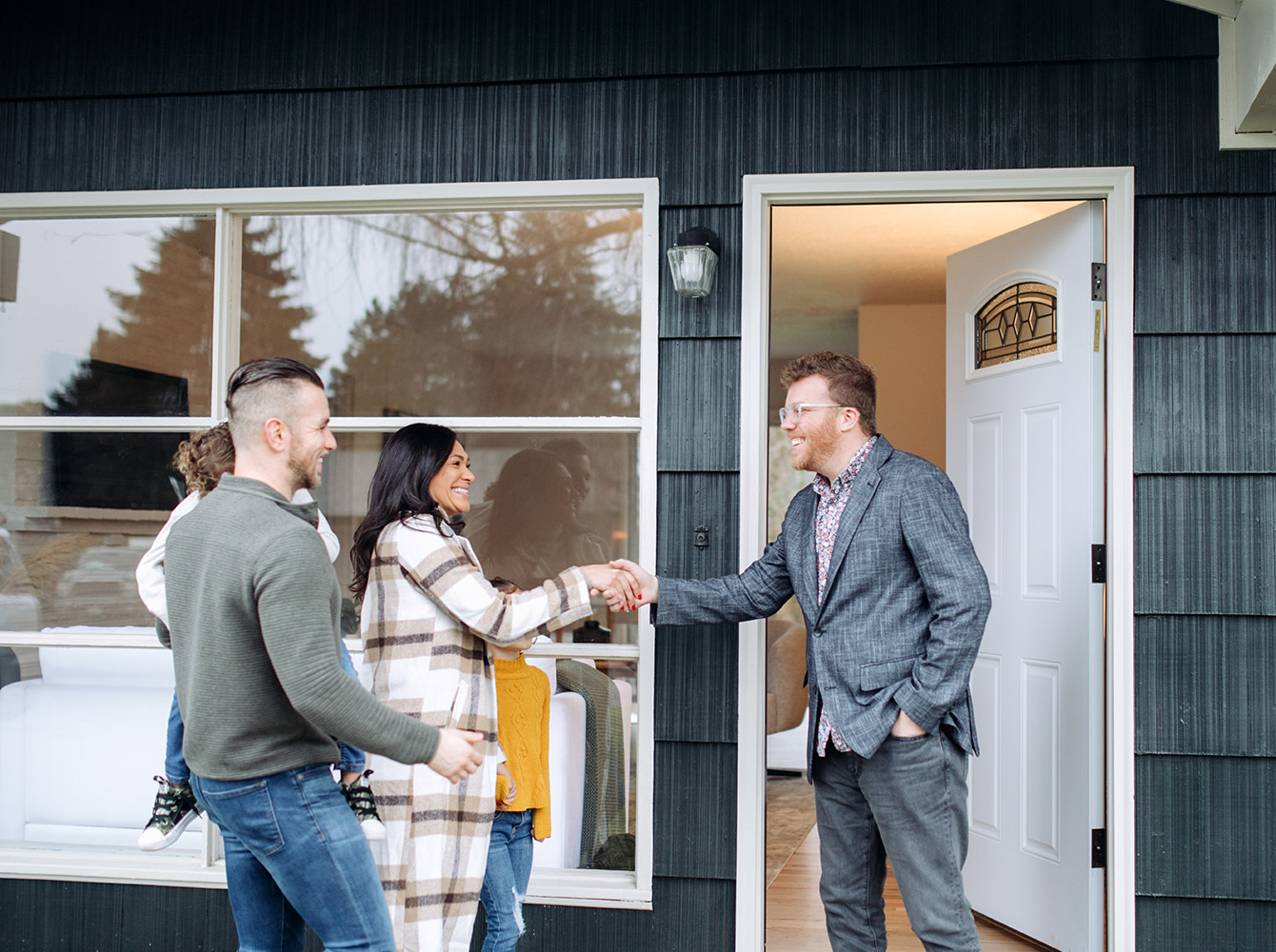 A realtor is shaking hands with a family at the front door of a house.