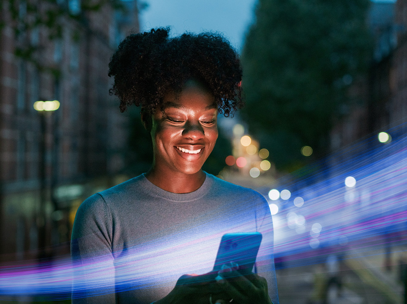 A woman is looking at her cell phone in her hands and smiling.