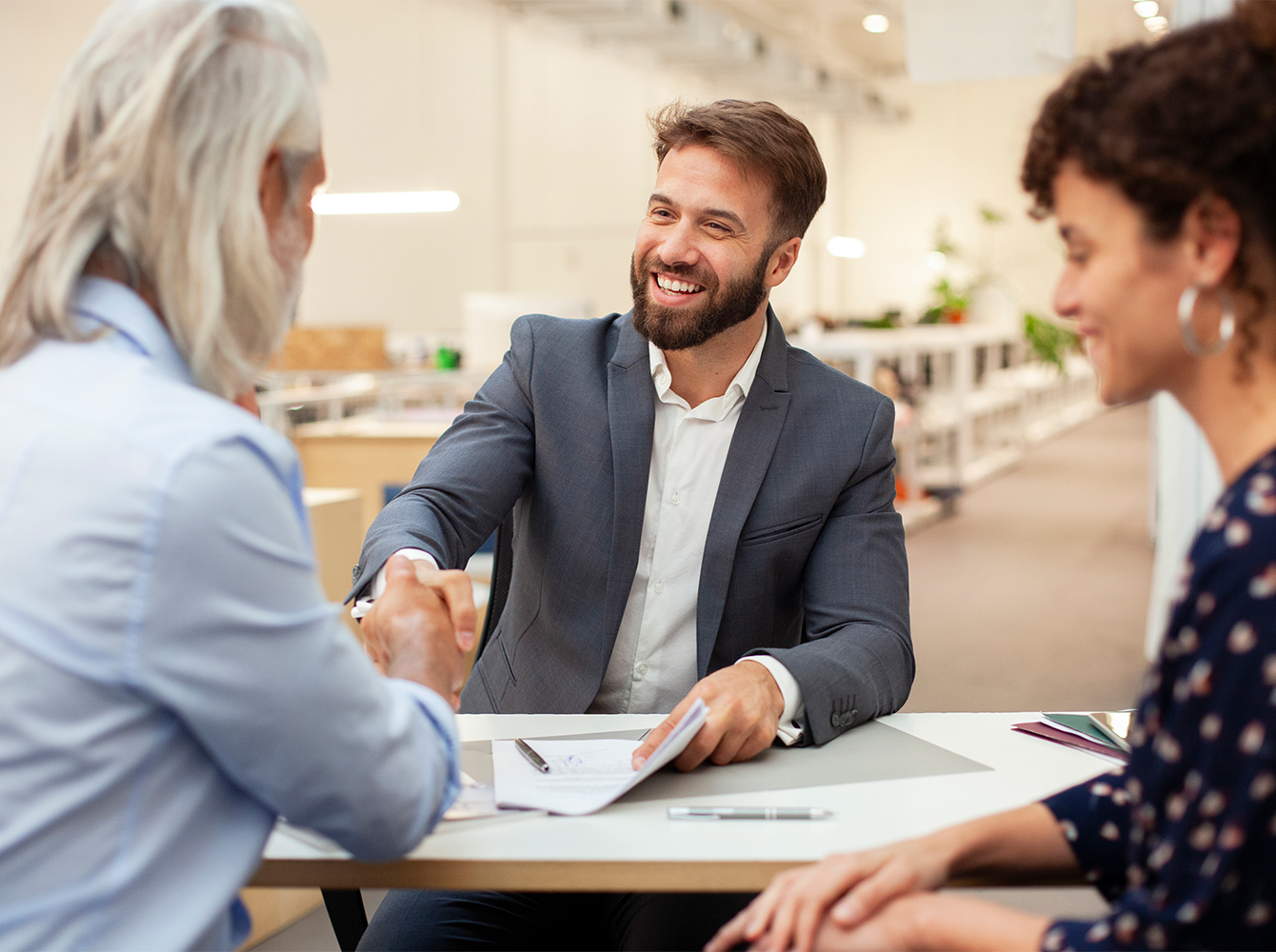 Three smiling people are sitting around a table with a contract on it.