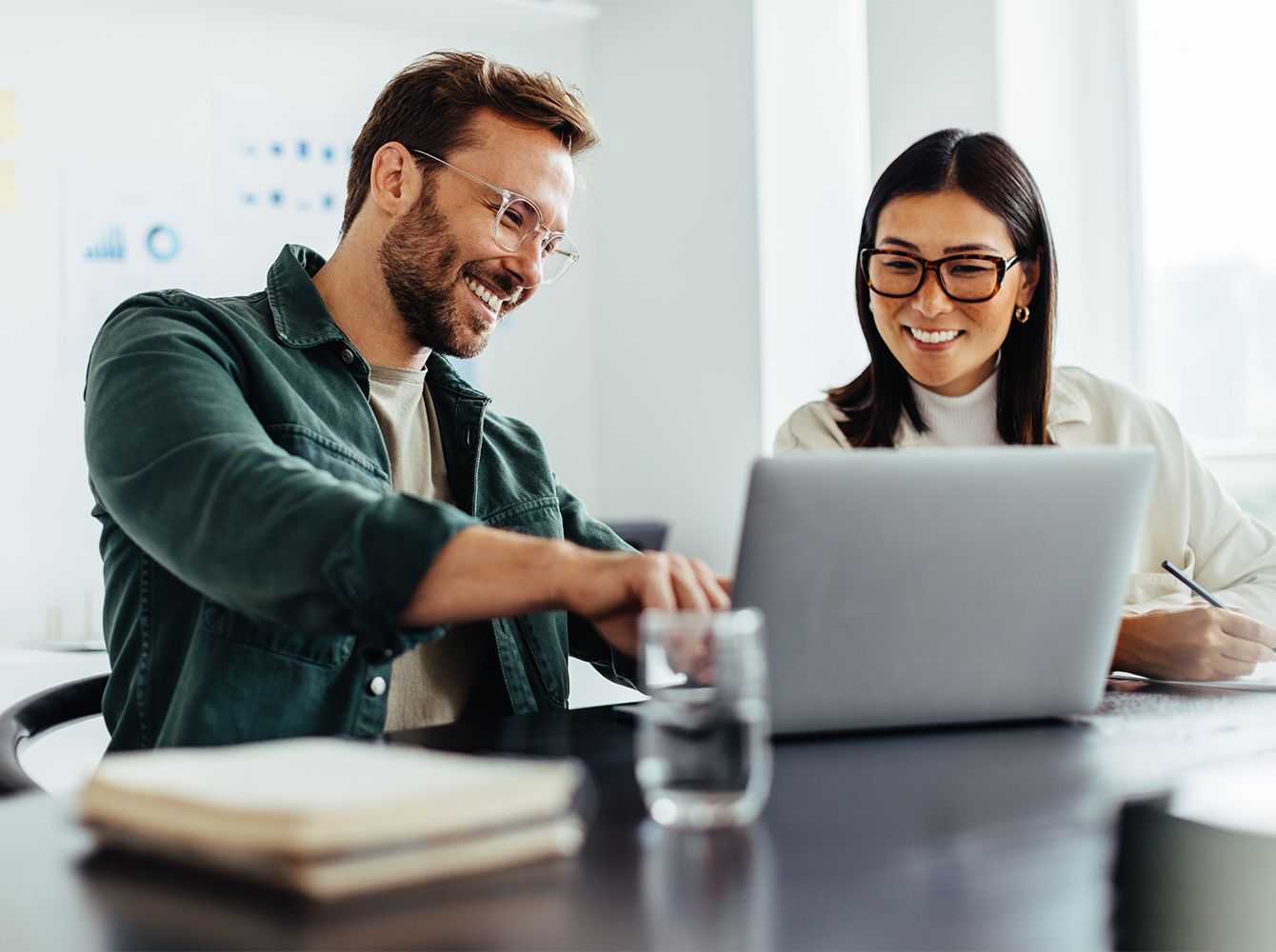 A smiling man and woman are sitting in a conference room, looking at a laptop.