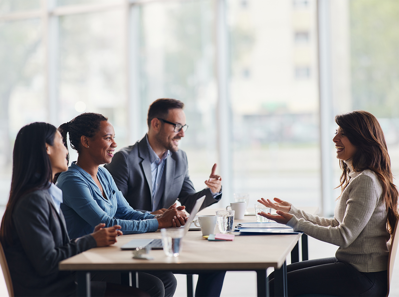 Four business professionals sit at a table having a discussion.