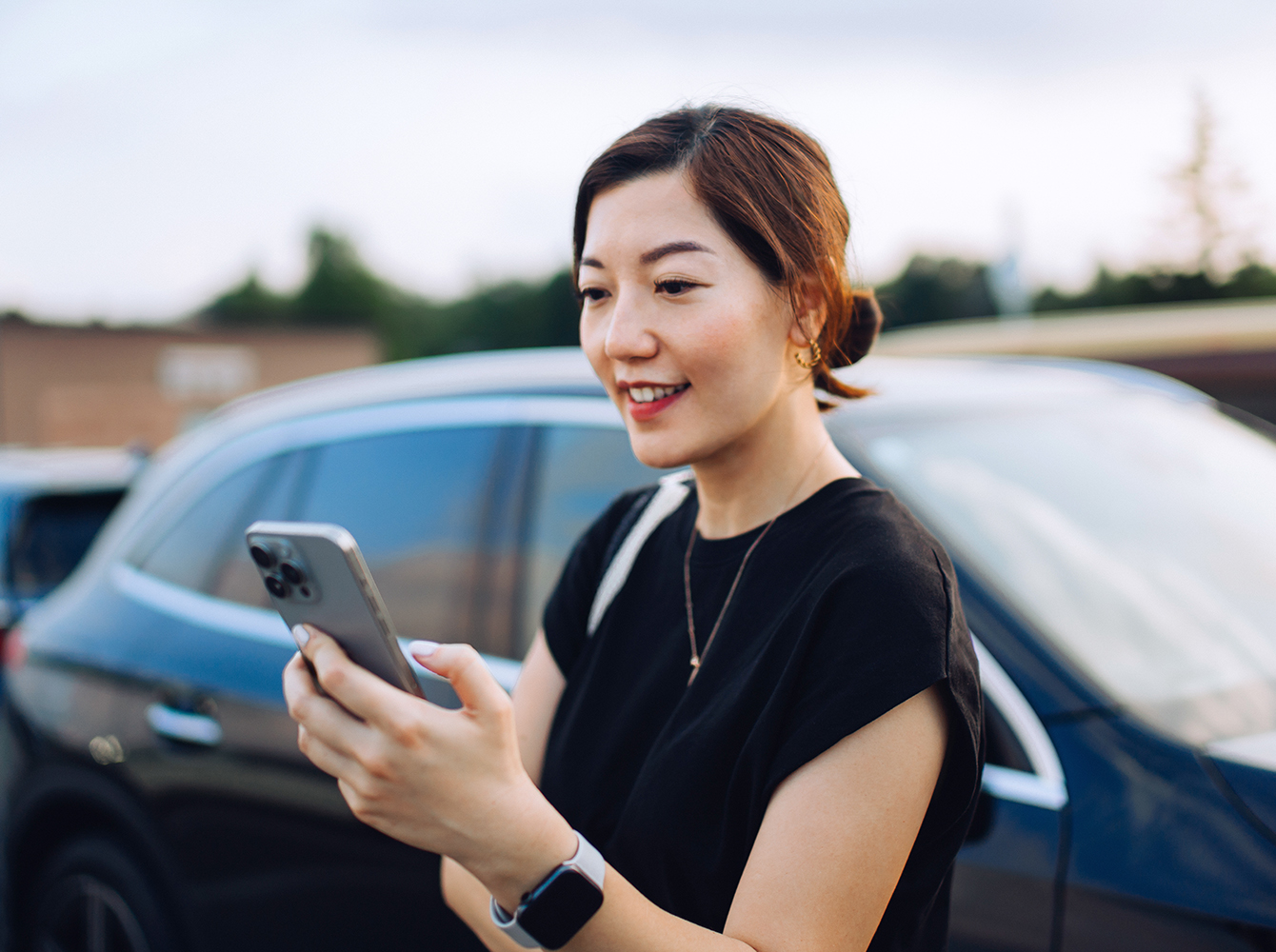 A woman is standing outside of her car looking at her cell phone.