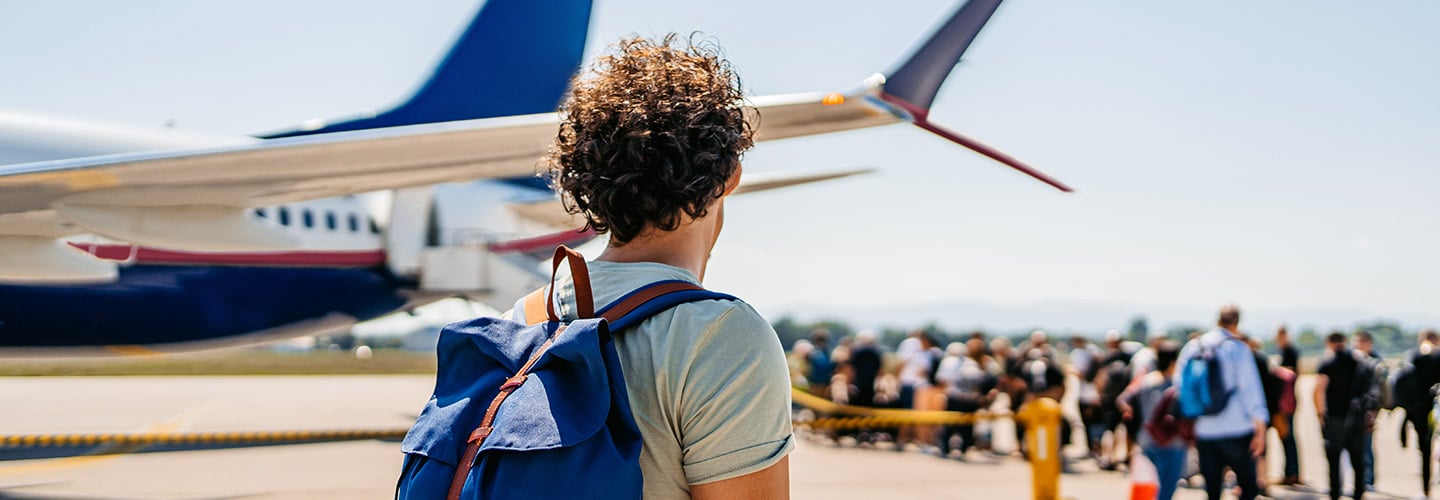 Man with a backpack on walking towards a crowd of people getting on a plane