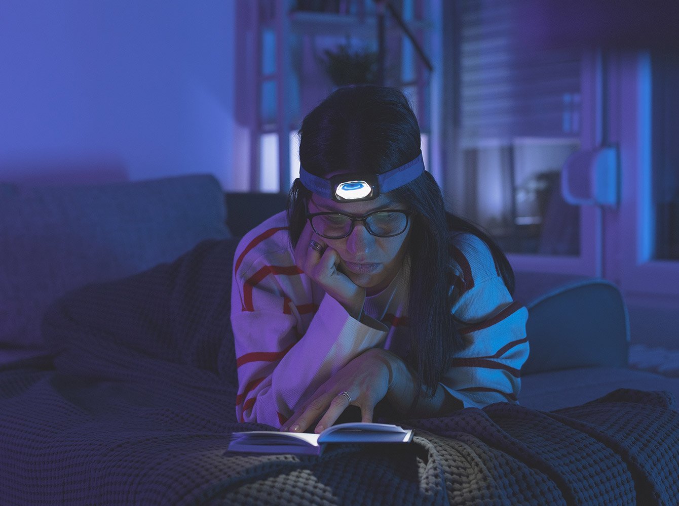 woman with a headlamp on sitting in the dark reading a book