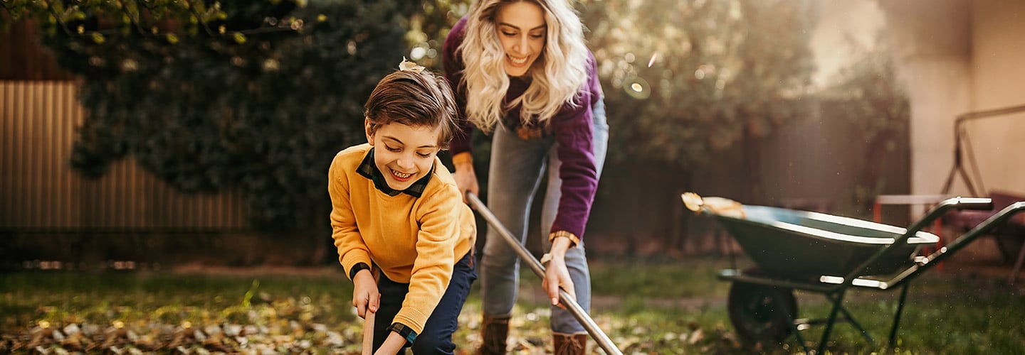 A woman and boy smiling and raking leaves