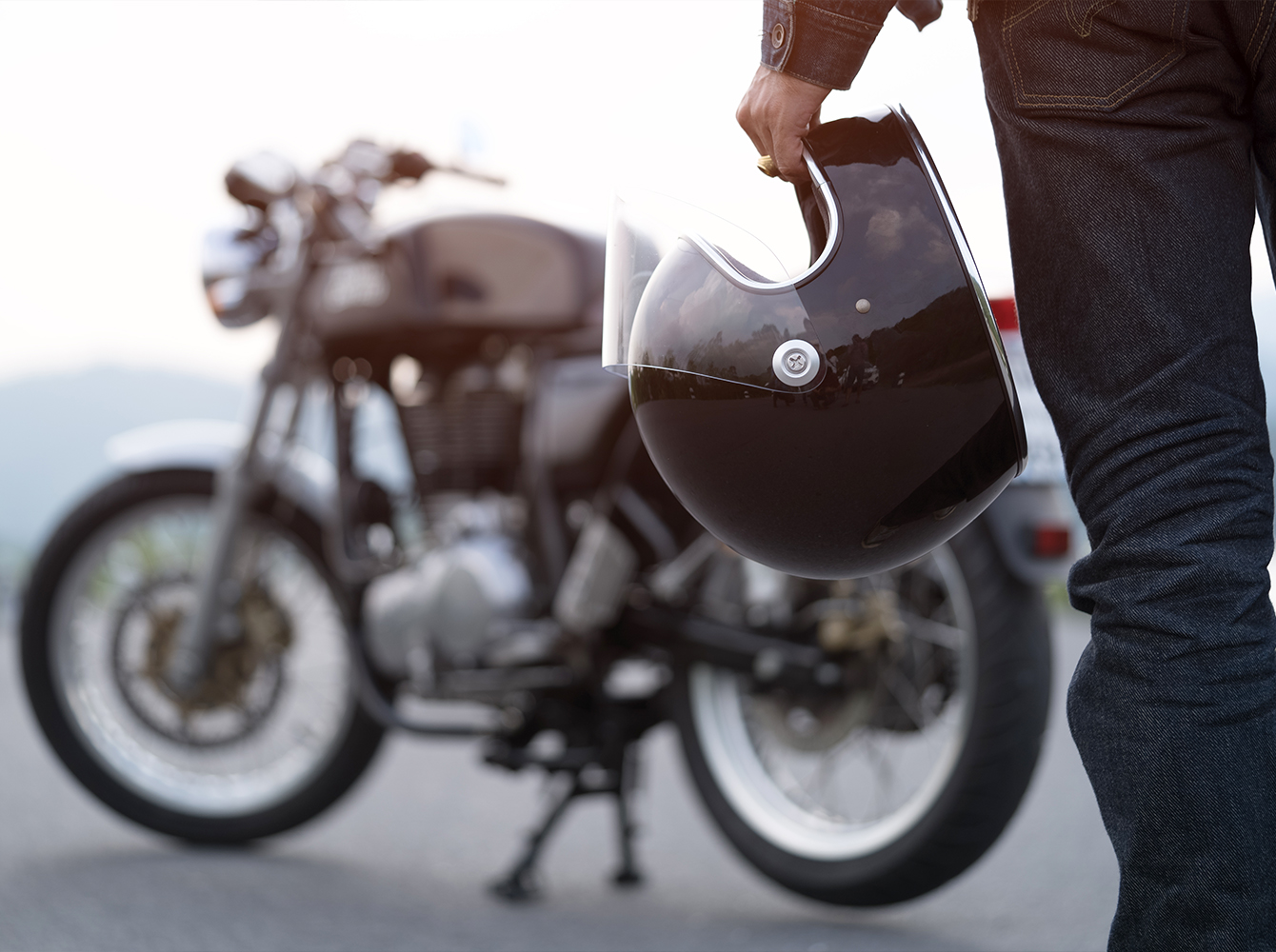 A person is walking towards a parked motorcycle with a helmet in their hand.