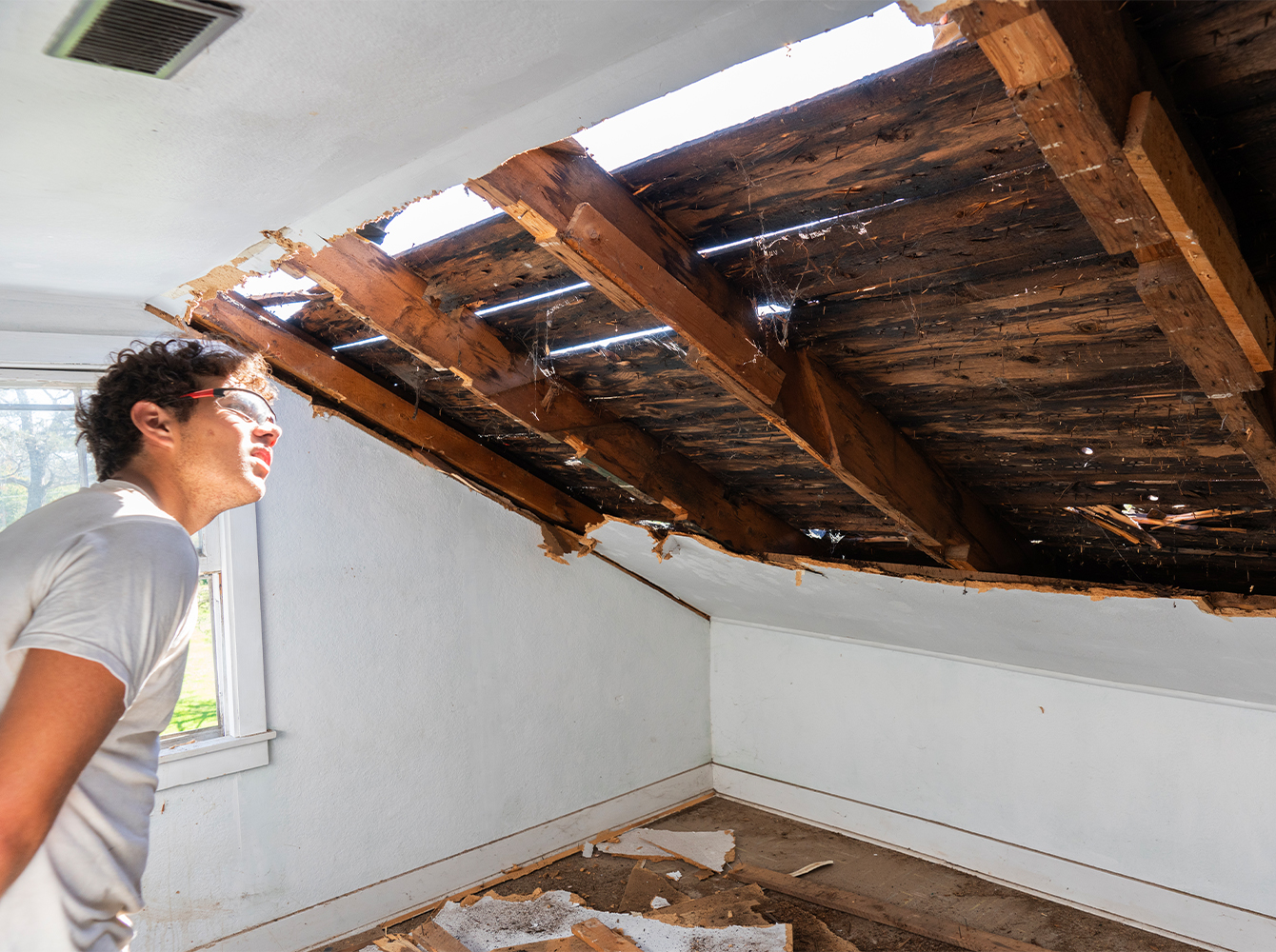 A man in safety glasses is looking at storm damage to a roof.