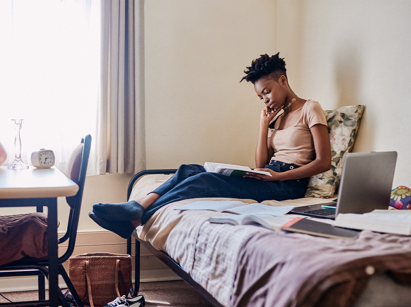 A college student is studying on their bed in a dorm room.