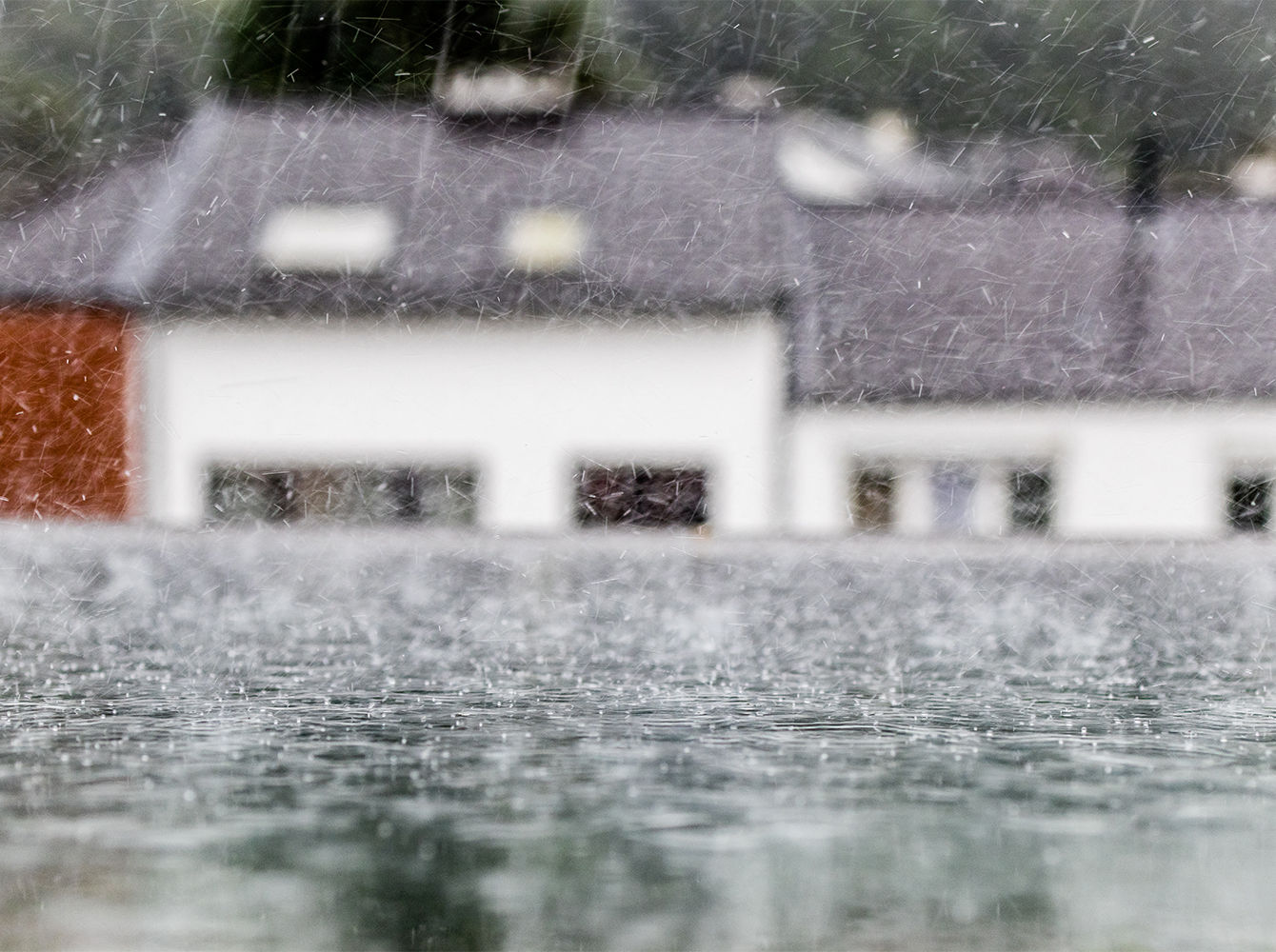 Sleet is falling on the roof of a house and there is another house in the background.
