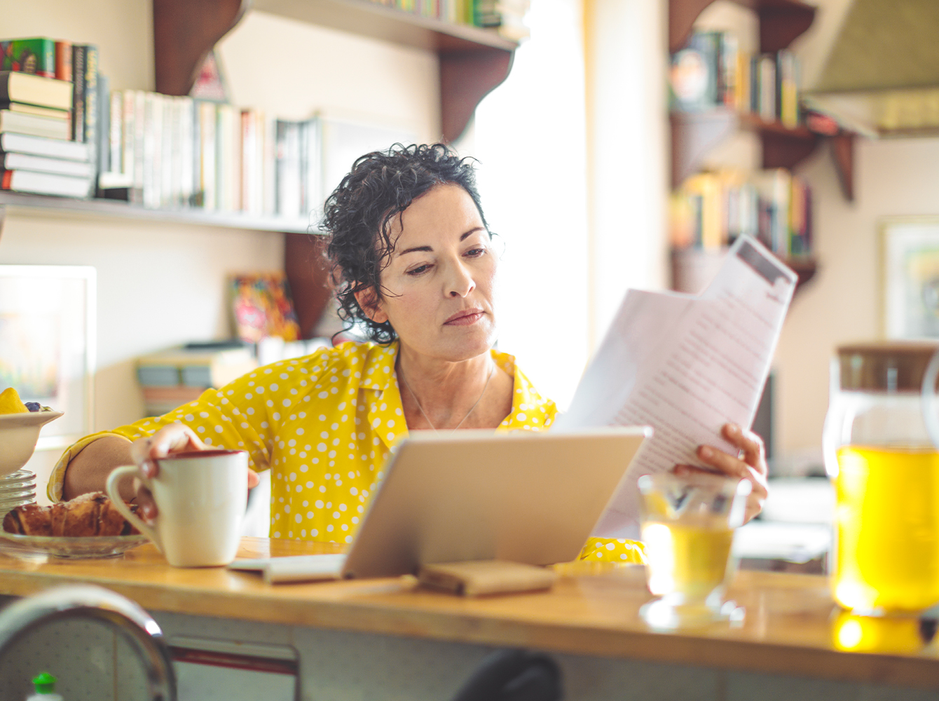 A woman is sitting at her kitchen table, working on her laptop.
