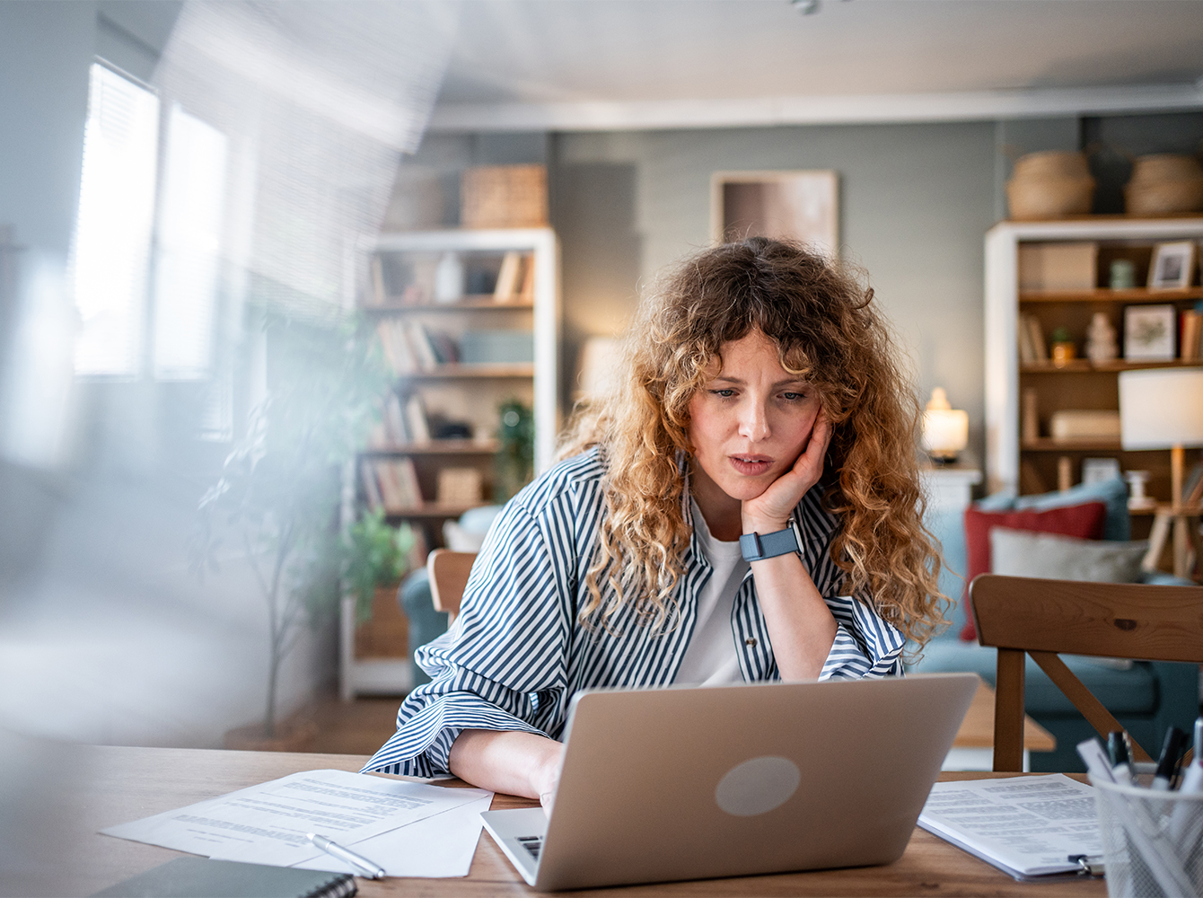A woman is sitting at a table looking at a laptop.