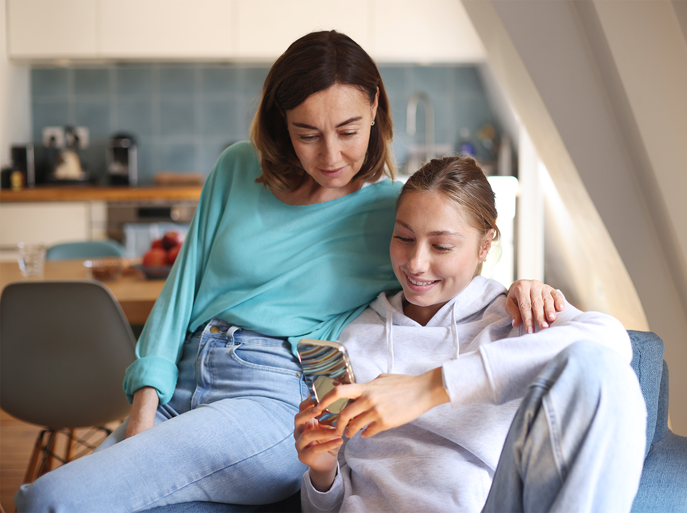 A mother and daughter are smiling and looking at a cell phone.