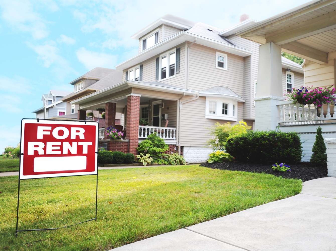 Houses on a street, with a for sale sign in the lawn of the closest house.