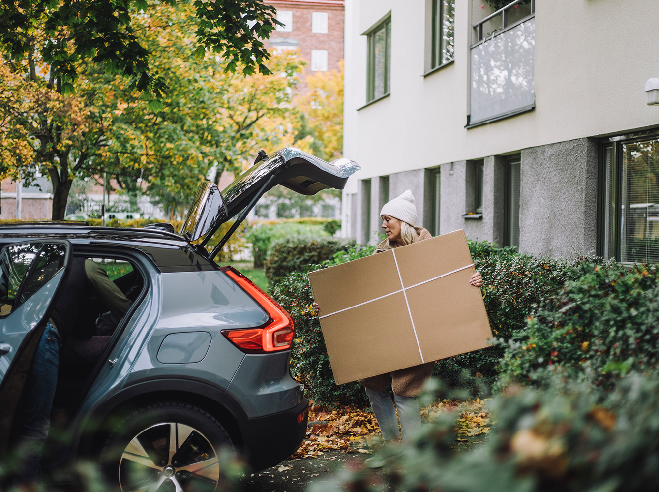 A woman is packing a large bundle into the back of a vehicle.