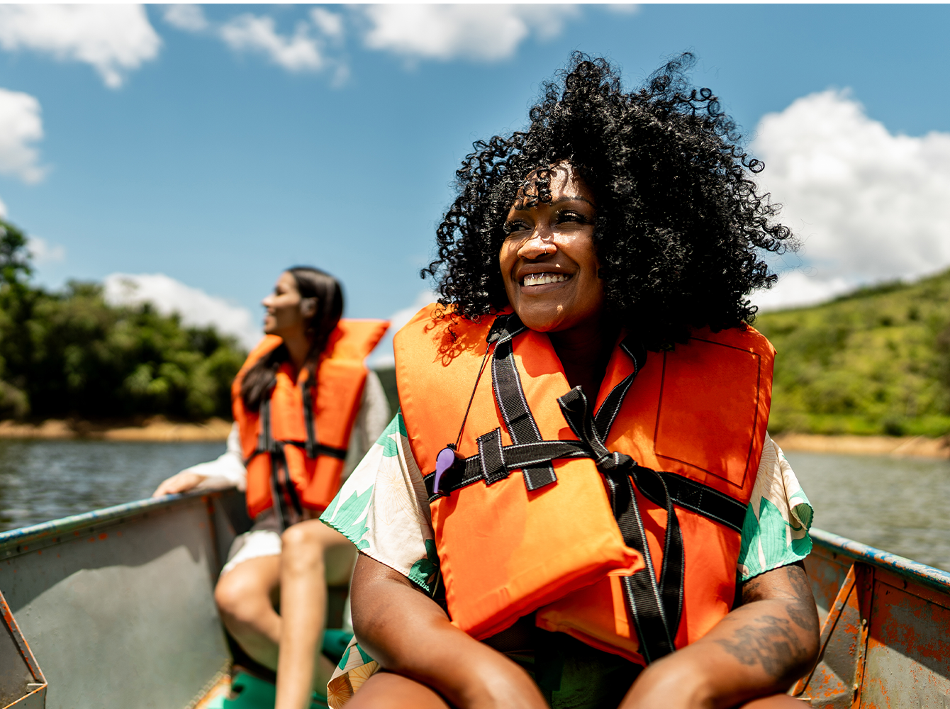 Two smiling women with life jackets on are in a boat on the water.