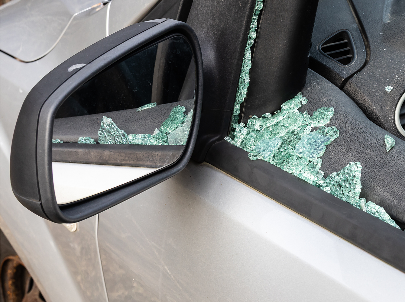 A car window is smashed in with broken glass in the driver's seat.