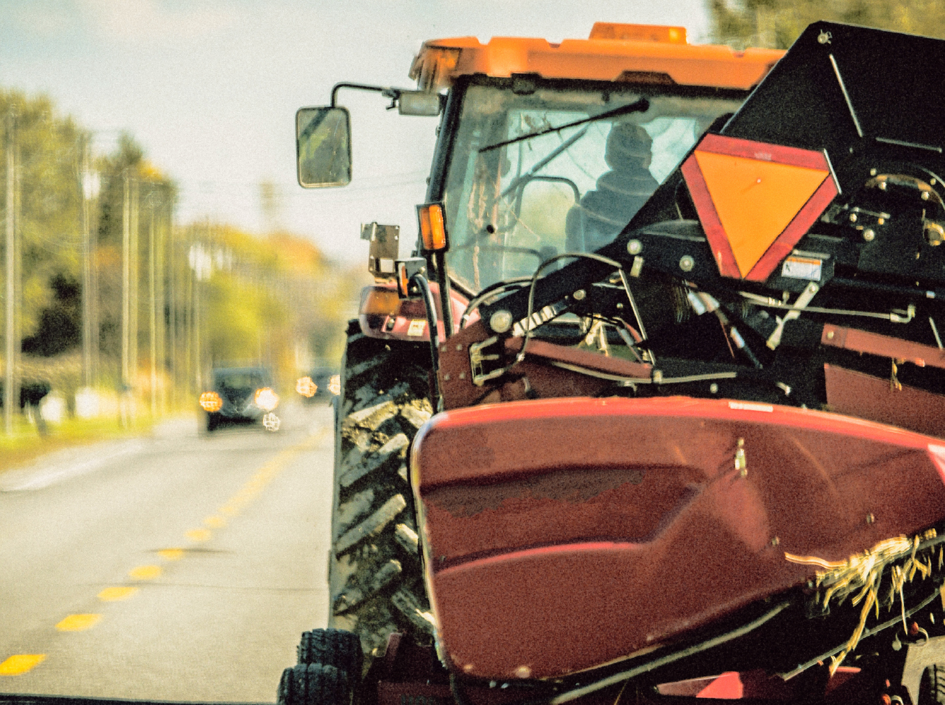 A large red tractor with a slow-moving vehicle sign drives on a rural road with oncoming traffic visible ahead.
