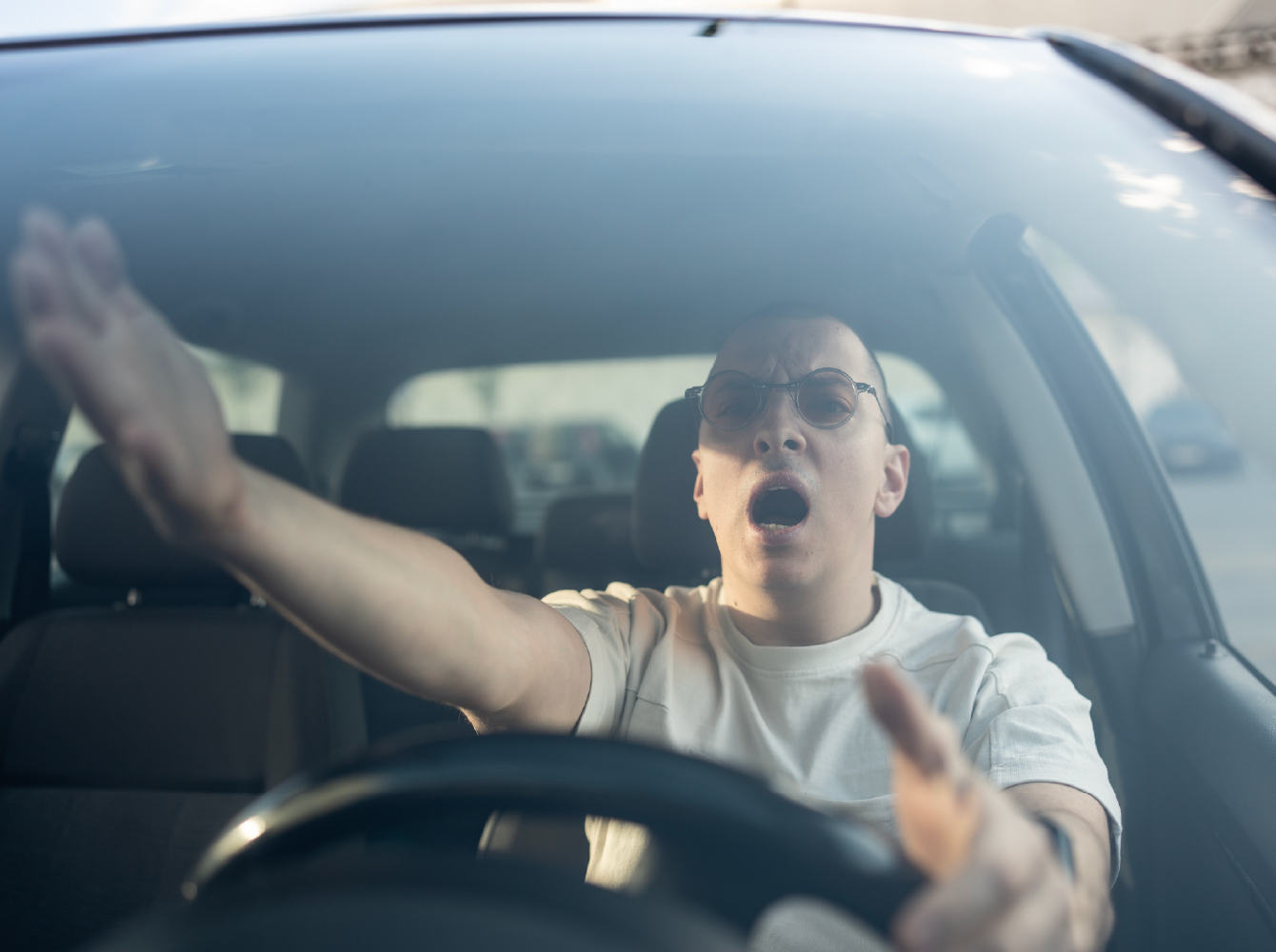 An angry driver shouting and gesturing with both hands off the steering wheel.
