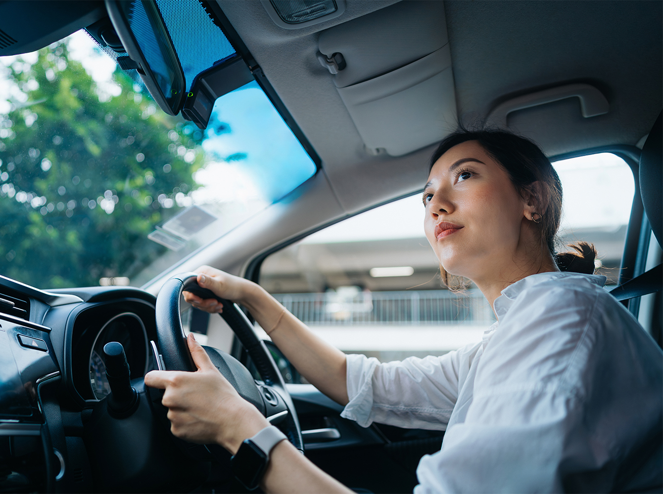 A woman is behind the wheel of a car on a nice day.