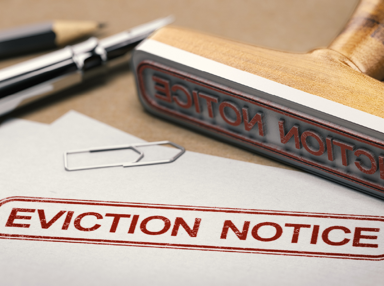 A desk with a pen, paperclip, a large stamp and a paper with the stamp that says EVICTION NOTICE.