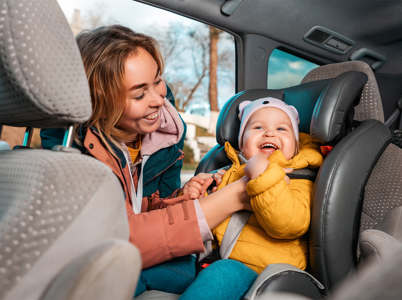A woman buckles a baby into a front facing car seat in the back of a car.