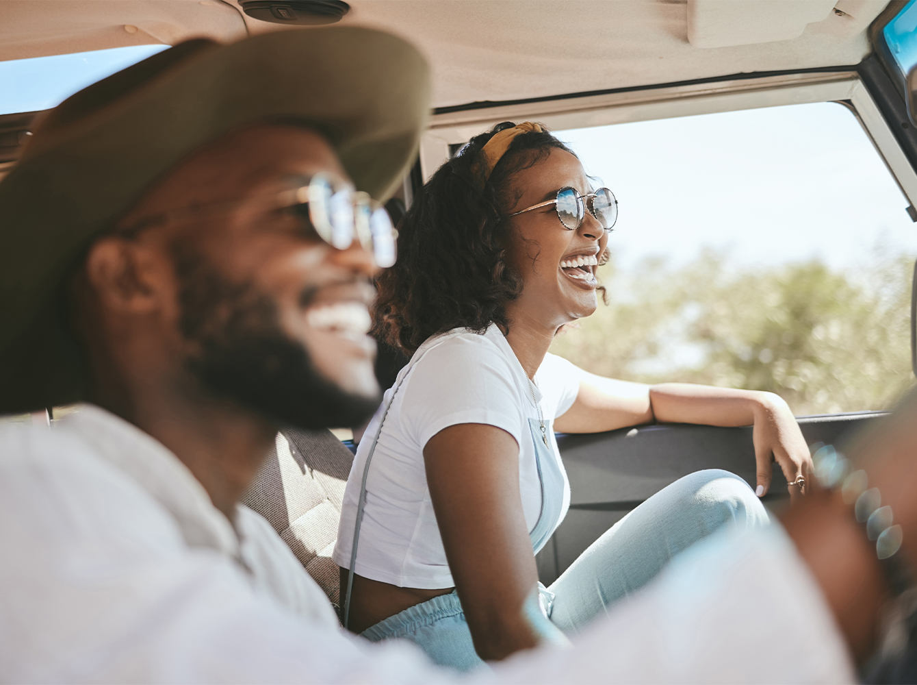 A smiling couple is driving in a car on a sunny day.