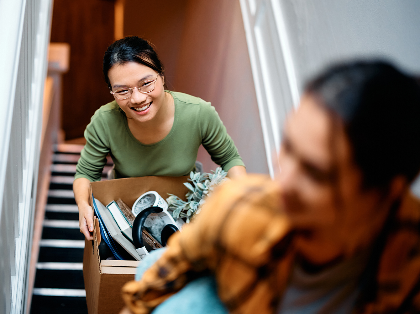Young people carrying household items up a flight of stairs.