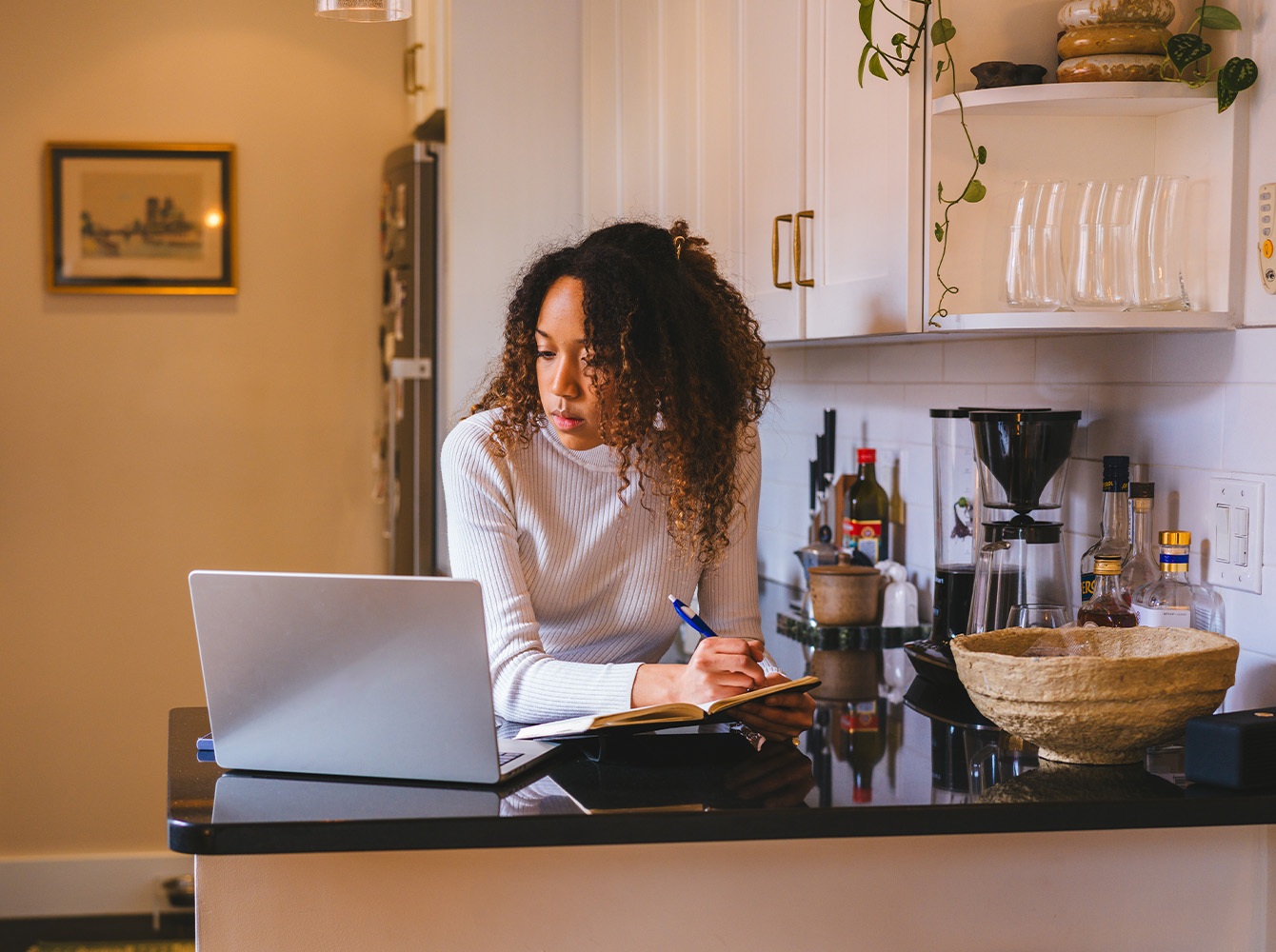 A woman is looking at a laptop resting on a kitchen counter.