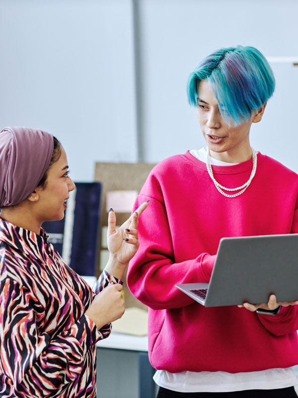 Two people talking an office, one of them is holding a laptop